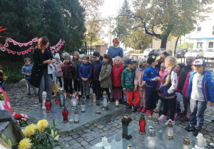Dzieci stoją z najstarszych grup przed pomnikiem, zapalanie znicza